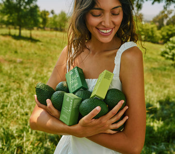 Woman holding avocados and Agave skincare products in a field